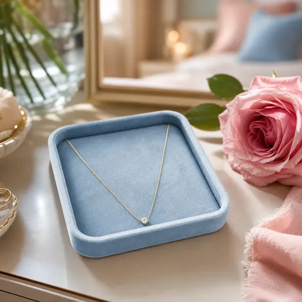 Delicate gold necklace on a velvet tray next to a pink rose